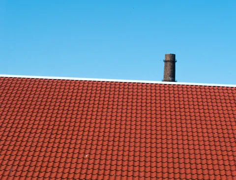 Impermeabilización en Berango: pide presupuesto. Tejado de teja roja con una chimenea y cielo despejado